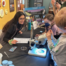 Aleezah helping kids look at sea slugs through the microscope at I Heart Science